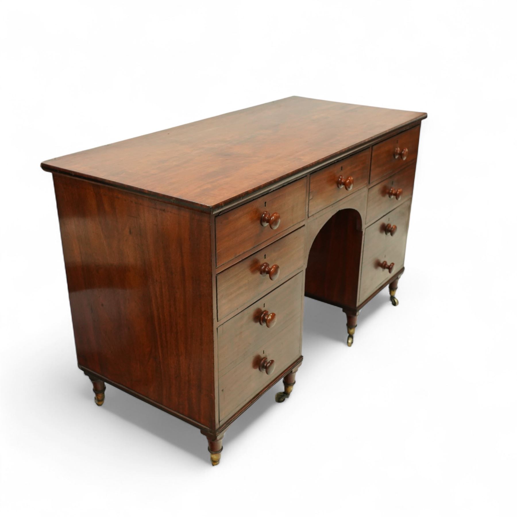 Early 19th century mahogany kneehole desk, rectangular moulded top over an arrangement of nine drawers with turned mahogany handles, arched kneehole recess, raised on short turned legs with brass cups and castors