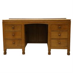Mouseman - adzed oak kneehole dressing table or desk, the rectangular adzed top with raised back and canted corners, over an arched recessed kneehole flanked by three graduating drawers to each side with turned knob handles, raised on octagonal feet, with carved mouse signature, by the workshop of Robert Thompson of Kilburn