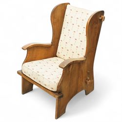 20th century pair of country lambing chairs in light oak, each with high winged back and shaped arms, pegged construction with panelled sides and arched aprons, loose seat and back cushions upholstered in cream floral fabric