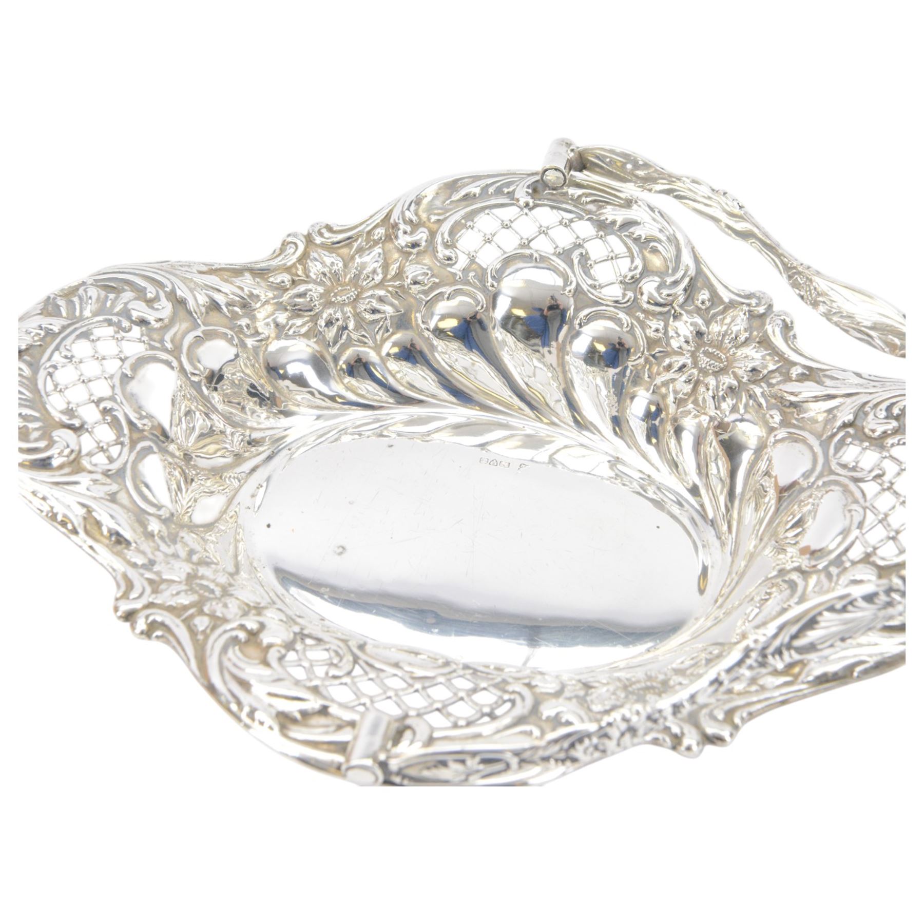 Edwardian silver swing handled basket, of oval form with shaped rim, embossed with floral decoration and with pierced latticework sides, upon four pad feet, hallmarked Chester 1905, maker's mark worn and indistinct