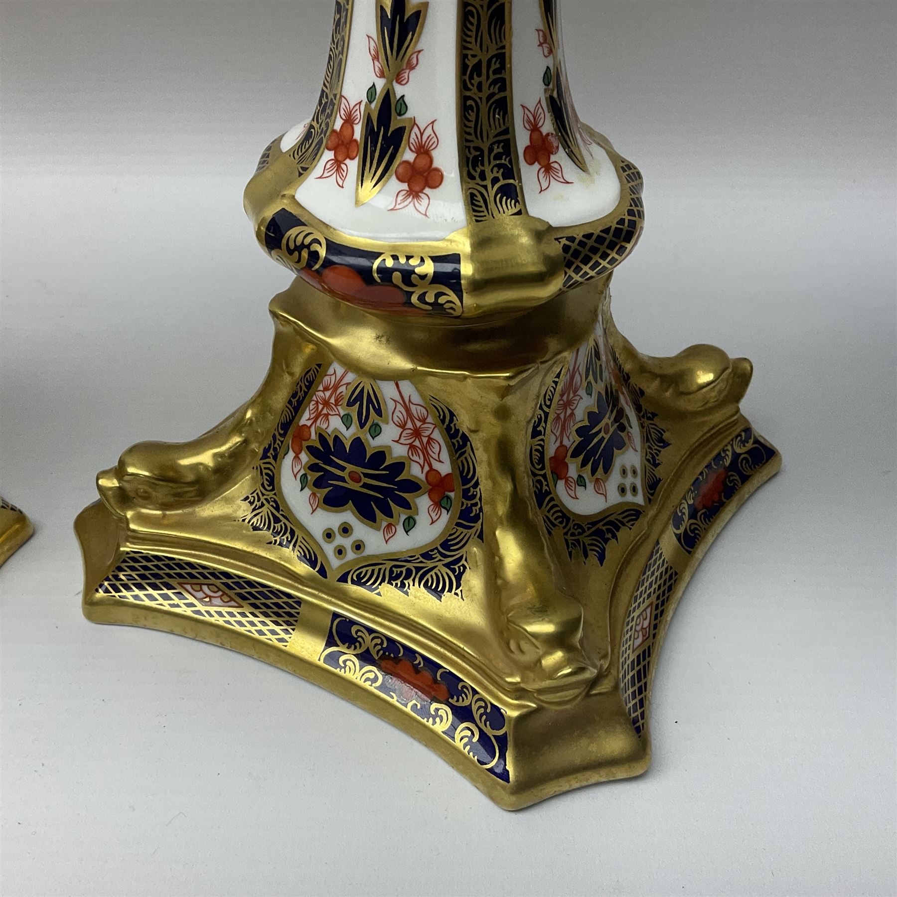 Pair of modern Royal Crown Derby Old Imari 1128 pattern candlesticks, each with shaped drip tray affixed to squat socket, upon spreading stem and canted square base with gilt dolphin edges, with printed marks beneath including Roman numeral year cypher for 2003, H26.5cm, with original boxes