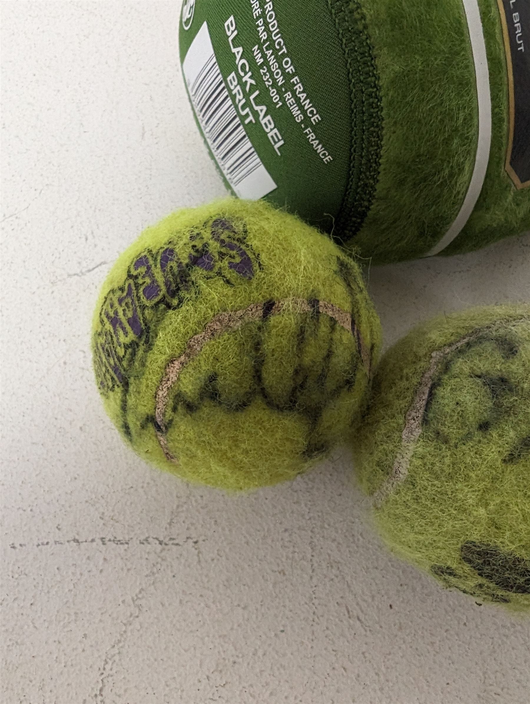 Three tennis balls, two with indistinct signatures, in Wimbledon Lansons Champagne cooler case