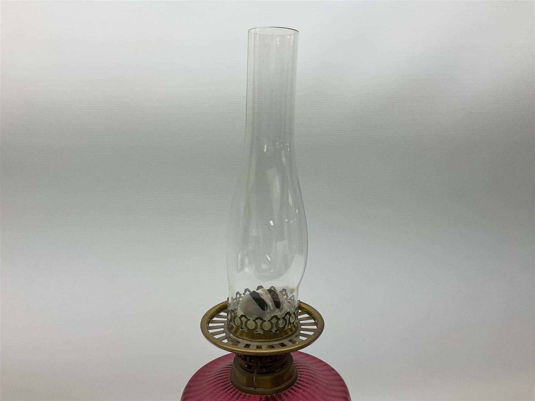 Victorian table standing oil lamp, brass fittings, cranberry glass reservoir, brass column on black enamelled ceramic base, with a frosted glass shade and clear glass chimney, H68cm