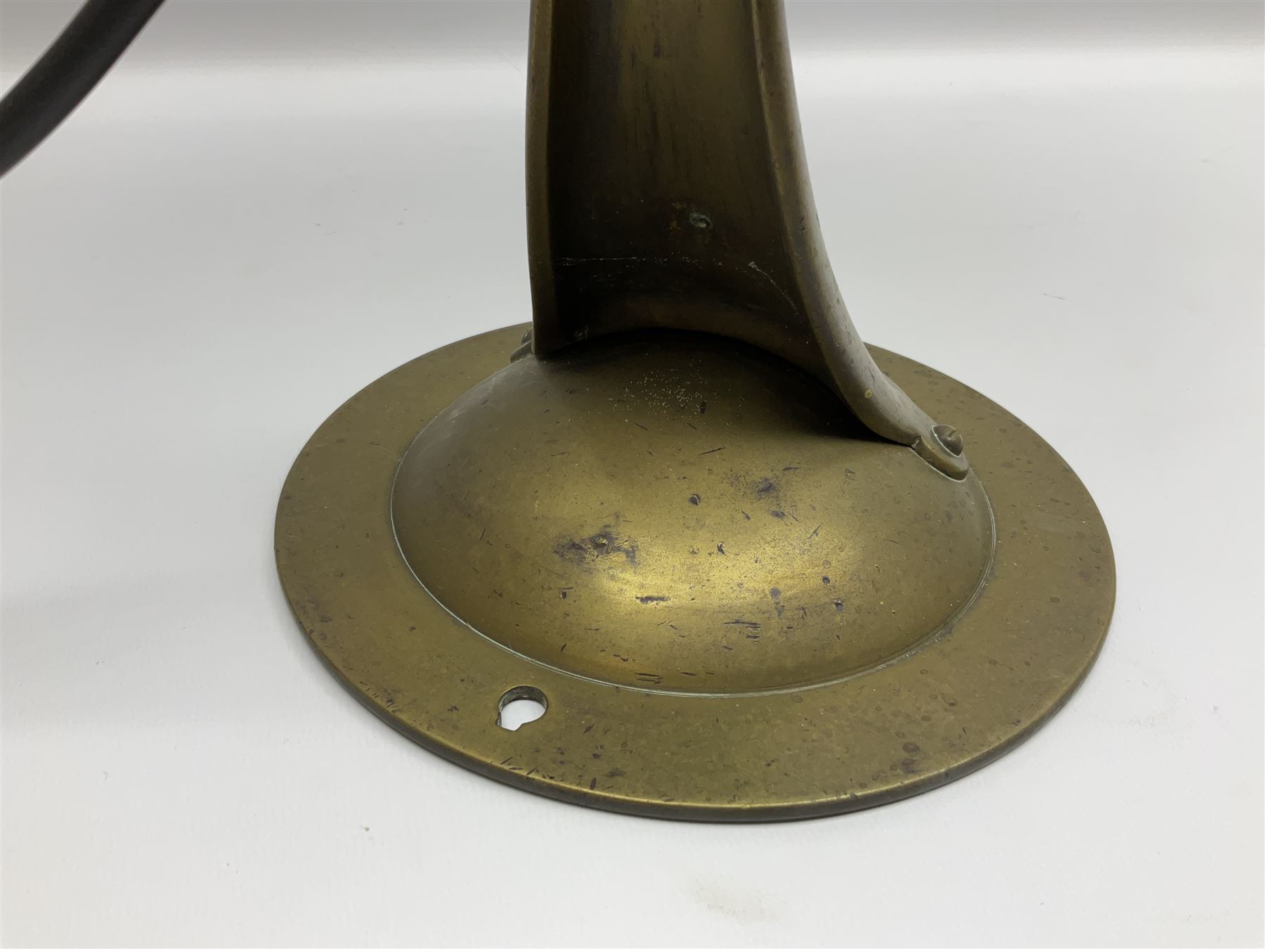 Arts & Crafts Jesson, Birkett & Co, brass table lamp or wall light, designed by Thomas Birkett, the tapering stem with adjustable ball pivot supporting a conical shade with tapering final with ball terminal, upon a circular domed base pierced for wall mounting, shade positioned upright overall H57cm

Often misattributed to Arthur Stansfield Dixon for Birmingham Guild of Handicraft, this particular lamp was designed by Thomas Birkett.
In the late 1890's Birkett worked as a metalwork at the Birmingham Guild, before later joining the Faulkner Bronze Company which went on to become Jesson, Birkett & Co in 1904. The lamp features in lighting catalogues from the firm under the model no E490.

