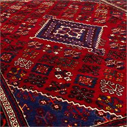 Central Persian Joshagan hand-knotted rug, madder-red field with central stepped lozenge medallion enclosed by angular spandrels, field decorated with repeating stylized geometric floral motifs and small diamond devices enclosed by a dark border of geometric ornament between multiple guard stripes, with cotton fringe ends  
