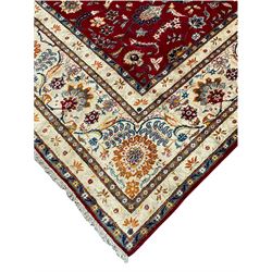 Large fine Persian Kashan carpet, the deep red ground field decorated with interlaced foliate and stylised plant motifs, seven band pale ivory ground border, the main band decorated with trailing foliate and flower head motifs of orange and blue