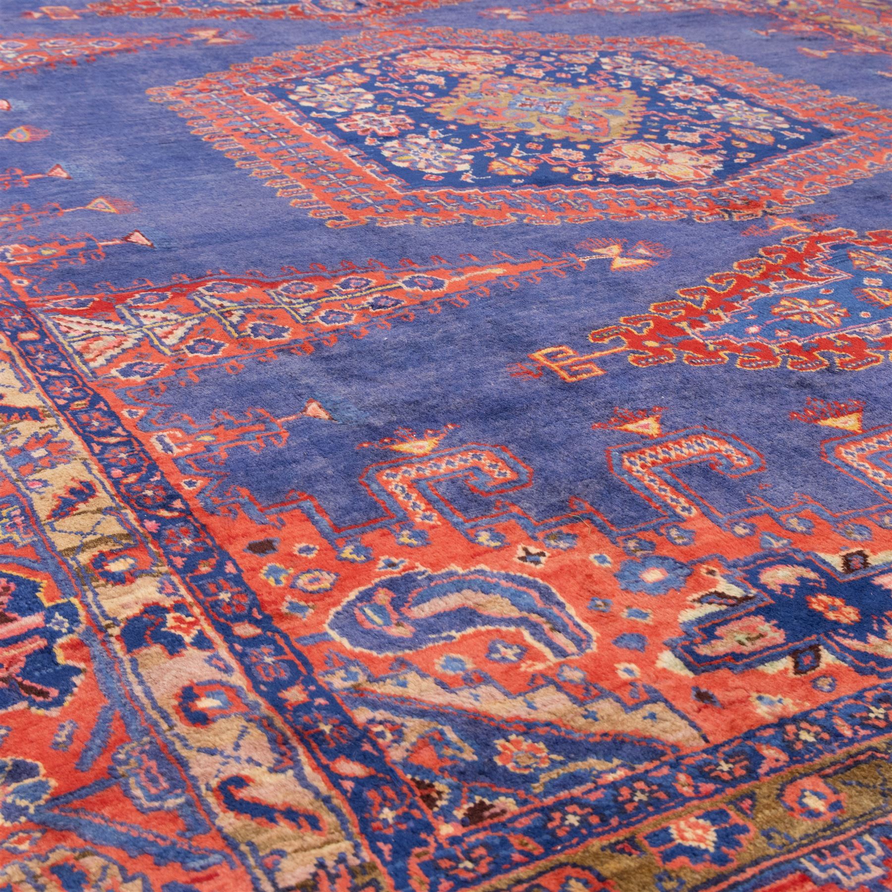 Central Persian Veis hand-knotted carpet, deep blue indigo field with central stepped lozenge medallion filled with stylized floral and geometric motifs, flanked by further angular medallions and tribal devices, edges with articulated and serrated hooked forms within a wide geometric border with repeating stylized floral motifs and multiple guard borders, in madder red, indigo blue, ivory, olive green, with cotton fringe ends