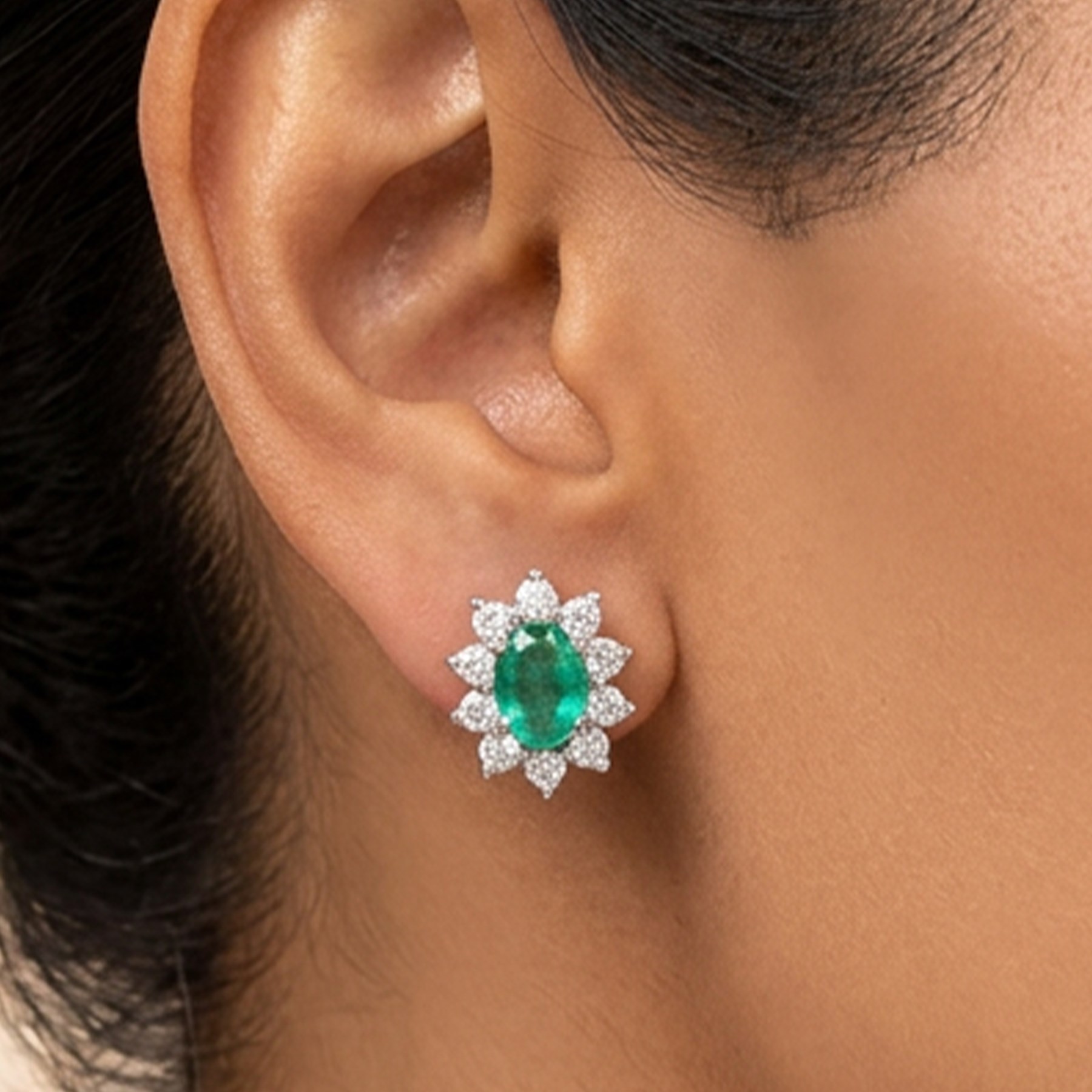 Pair of 18ct white gold emerald and diamond cluster earrings, each stud set with a single oval cut emerald surrounded by round brilliant cut diamonds, stamped, total emerald weight approx 0.75 carat, total diamond weight approx 0.55 carat