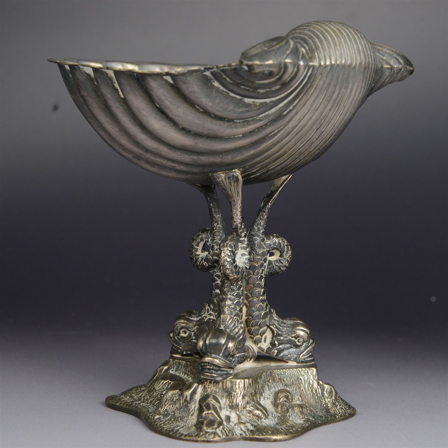 Pair of Victorian silver plated comports, with clam shell bowls supported by three dolphins upon a rocky base, H12cm