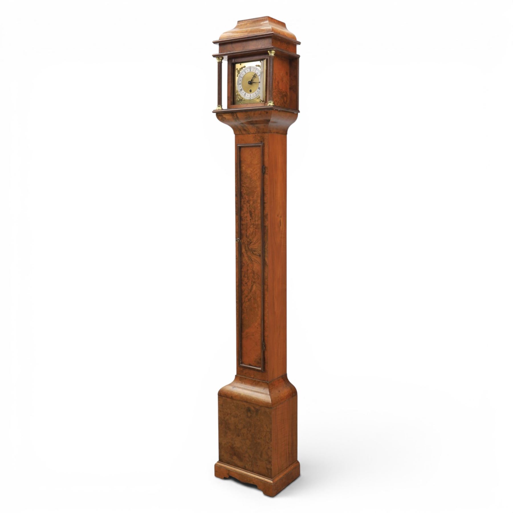Early 20th century walnut small longcase clock, brass dial with silvered Roman numeral chapter ring and pierced black hands, the figured walnut case with shaped projecting hood, long moulded trunk door and stepped plinth base