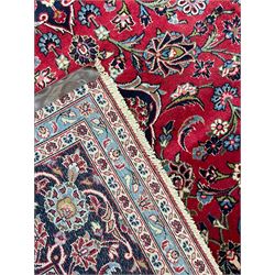 Central Persian Kashan carpet, red ground field with blue medallion and spandrels, decorated all-over with trailing foliate and stylised plant motifs, scrolling design border with guards