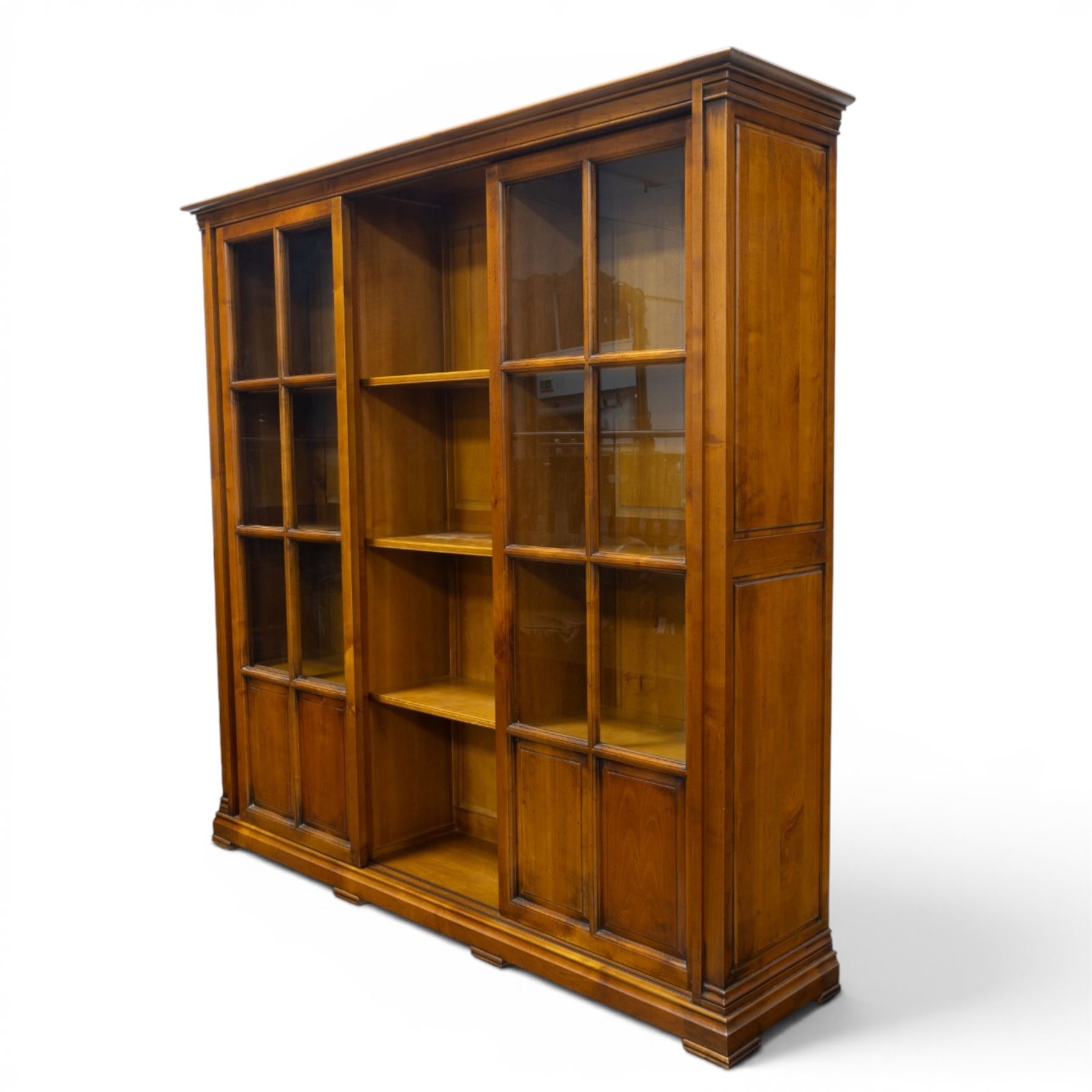 Wesley Barrel - large cherry wood bookcase, with projecting cornice and fielded panelled sides, with three sections comprising three fixed shelves, sliding glazed and panelled doors, moulded plinth base