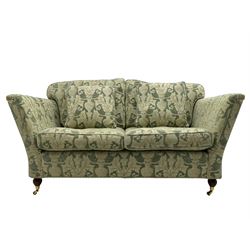 Pair of Edwardian design two-seat sofas, upholstered in urn and curled acanthus leaf patterned fabric, on turned feet with brass cups and castors 