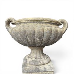 Pair of Neoclassical design weathered cast stone garden urns of kylix form, the rolled rim flanked by twin pierced scroll handles over a shallow gadrooned bowl, raised on a fluted circular socle and faux panelled square pedestal base