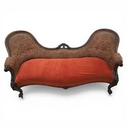 Victorian mahogany framed serpentine sofa, the shaped button upholstered back with central carved foliate cartouche, and scroll arms with carved terminals, over upholstered red seat, upon carved cabriole supports with castors