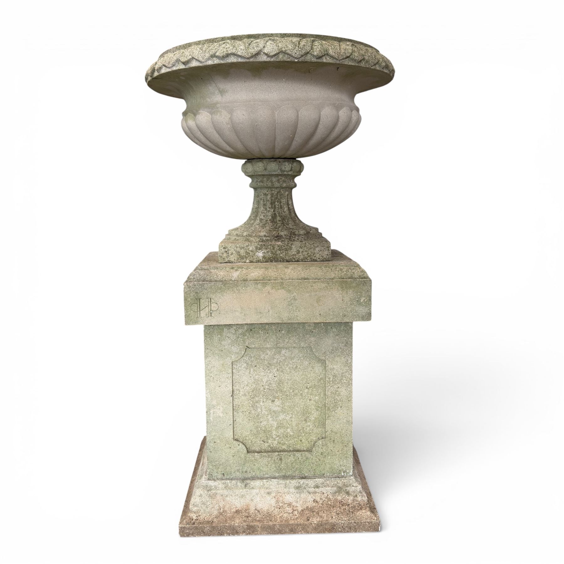 Pair of weathered cast stone Neoclassical design garden Kylix shape urns, foliate moulded rim over a gadrooned underbelly, the scalloped socle over a rectangular pedestal with faux-panelled sides, stamped with stylised ‘H’ monogram
