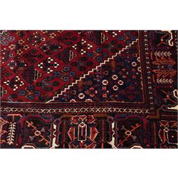 Central Persian Joshaghan hand-knotted carpet, deep red field decorated with a lattice design of stylized boteh and palmette motifs arranged around a stepped diamond medallion, navy corner spandrels similarly decorated enclosed by a dark indigo main border of floral and geometric motifs between multiple guard stripes, with cotton fringe ends 