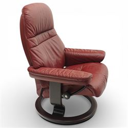 Ekornes - Stressless reclining armchair and matching footstool, upholstered in oxblood leather with padded headrest and segmented back cushion, shaped armrests with exposed adjustment handles, raised on stained laminated beech circular swivel base, the conforming stool on matching ring base