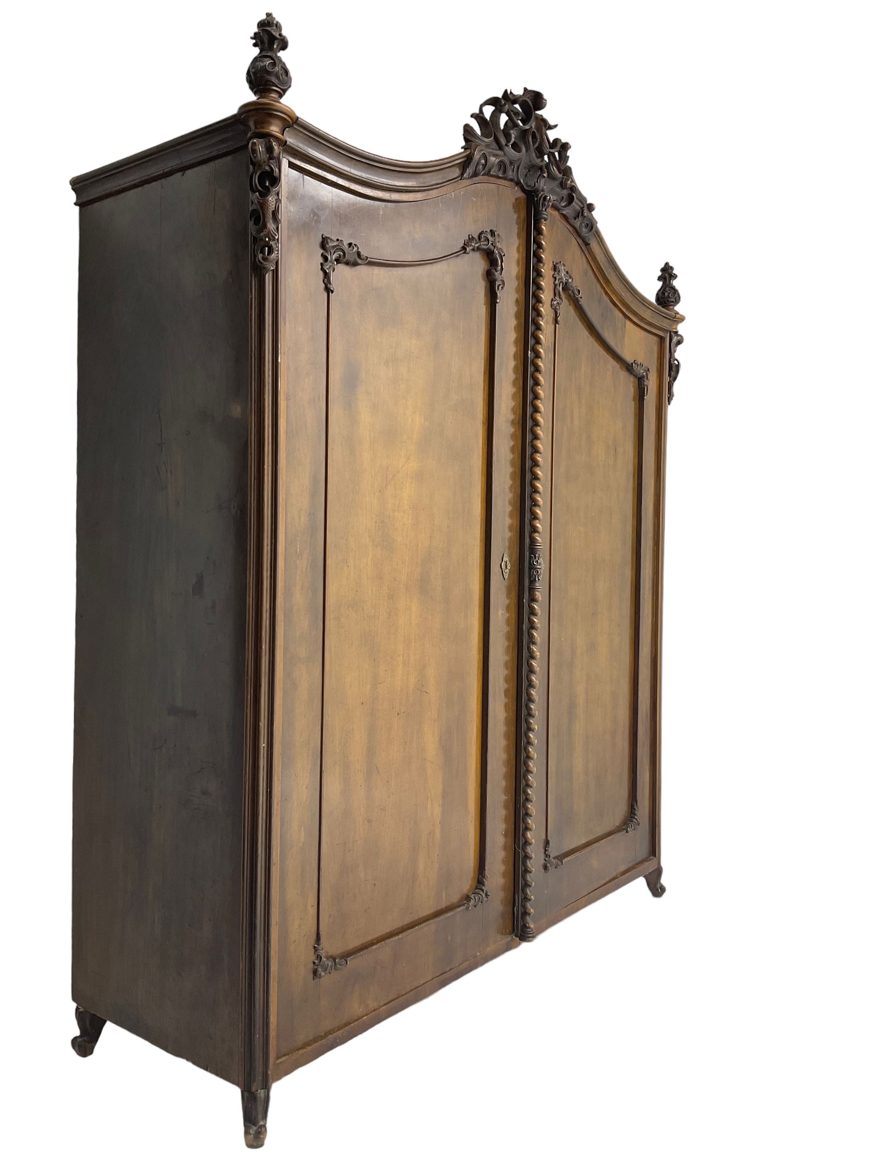 Early 20th century Italian walnut armoire wardrobe, the pierced and scrolling pediment carved with acanthus leaf detail, flanked by two scrolling cartouche with matching corbels below, the two panelled doors with applied carved rinceaux slips, with a central spiral turned upright, enclosing single shelf and hooks, raised on scroll feet