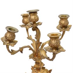 French-Late 19th century 8-day gilt brass rococo style mantel clock, c1890, waisted case  decorated with scroll work, leaves and musical instruments, resting on an attached plinth with splayed feet, dial within a glazed brass bezel with a gilt repoussé centre, porcelain cartouche Roman numerals and steel fleur-di-Lis hands, with a twin train movement, recoil anchor escapement and countwheel strike, sounding the hours and half-hours on a bell. With a matching pair of five-light candelabra. No Pendulum or Key.