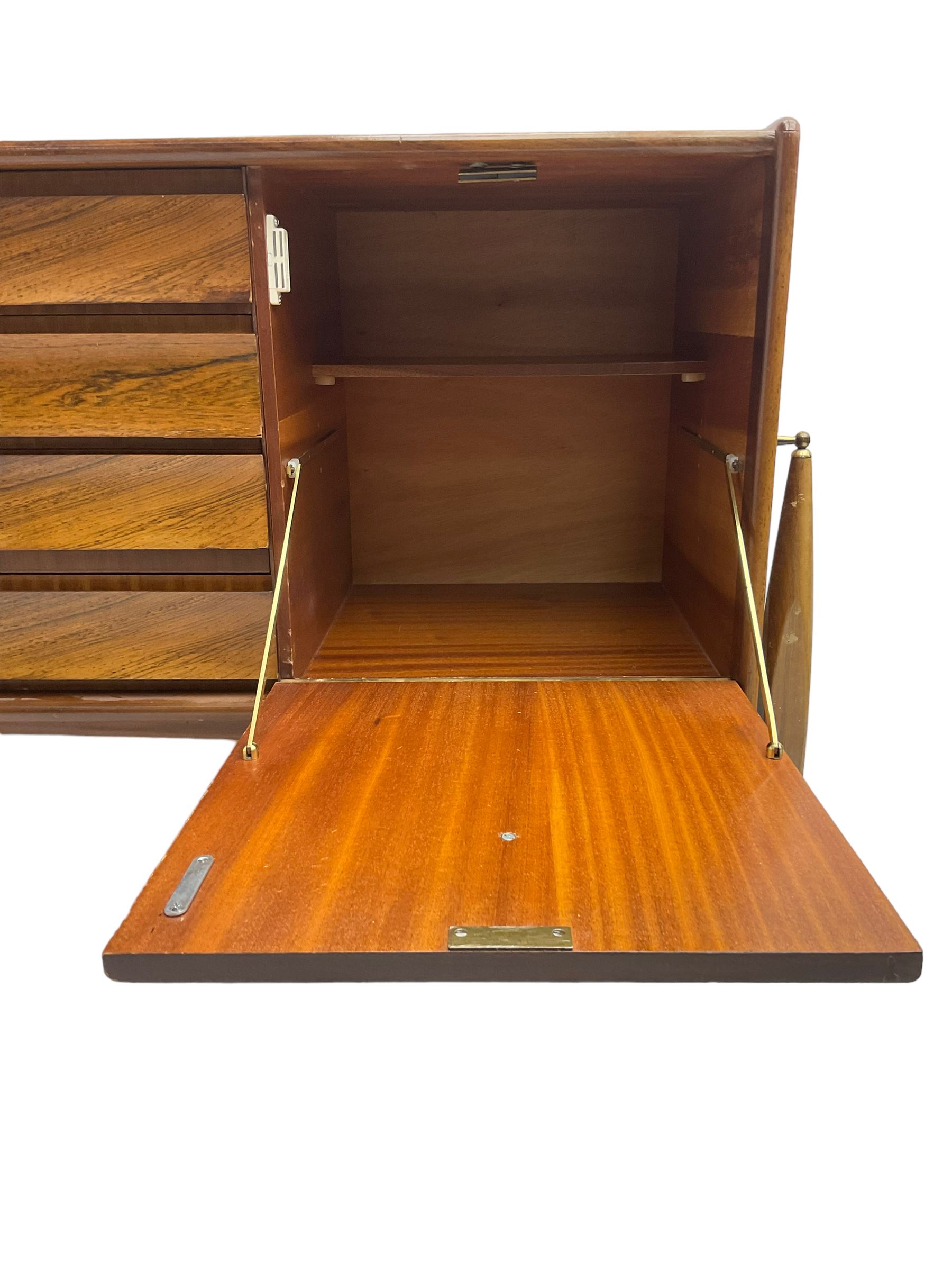 Elliots of Newbury (EoN) - mid-20th century teak sideboard, fitted with four central doors flanked by fall-front cupboard and a double cupboard, each with concave wooden handles