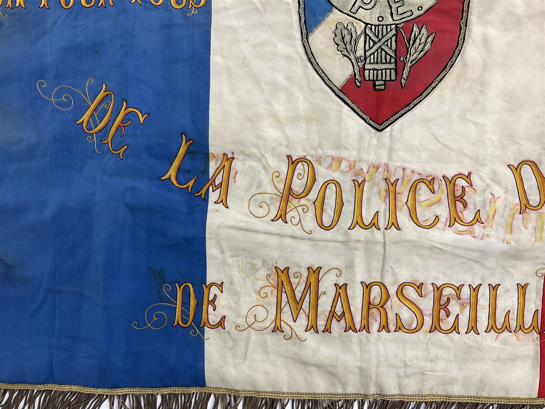 French State Police banner as the tricolor flag embroidered with coloured and metallic thread 'Societe De Secours Mutuels Un Pour Tous Tous Pour Un De La Police D'Eteat De Marseille' to one side; plain flag verso; tassels to three sides 100 x 113cm