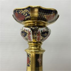 Pair of modern Royal Crown Derby Old Imari 1128 pattern candlesticks, each with shaped drip tray affixed to squat socket, upon spreading stem and canted square base with gilt dolphin edges, with printed marks beneath including Roman numeral year cypher for 2003, H26.5cm, with original boxes