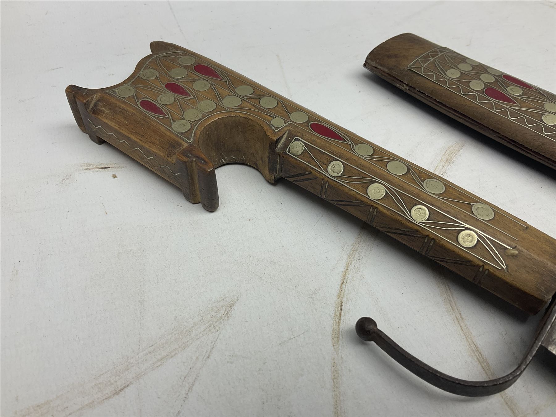 Late 19th/early 20th century Moroccan nimcha dagger-sword, the 40cm curving steel blade with engraved decoration on both sides; shaped hardwood hilt inlaid with brass, white metal wires and red coloured panels; in similarly inlaid scabbard L61cm overall