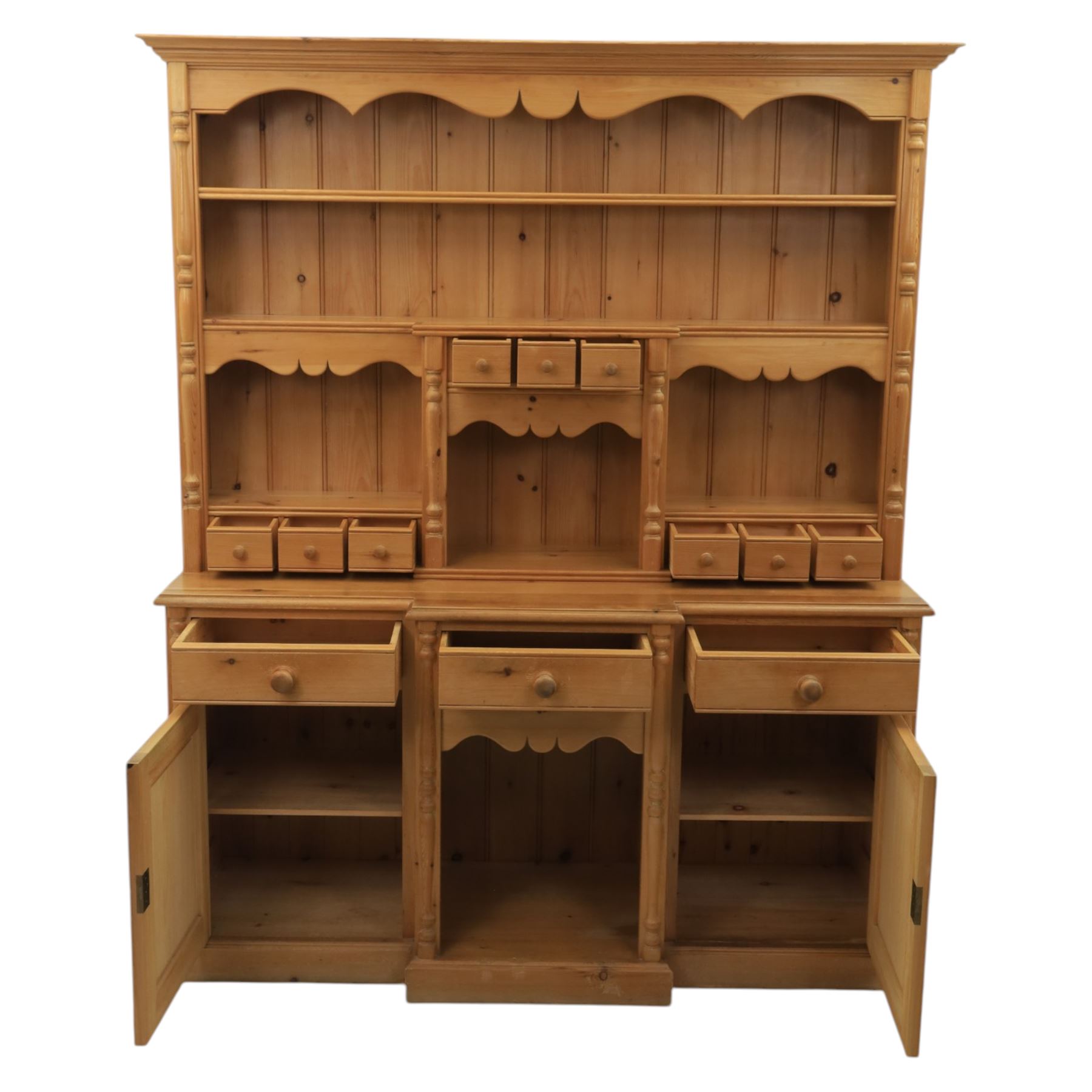 20th century country style waxed pine housekeeper’s cupboard, upper section with moulded cornice, shaped aprons and open shelving around central drawer arrangement, the lower section fitted with three drawers and two cupboards with panelled doors, raised on a plinth base