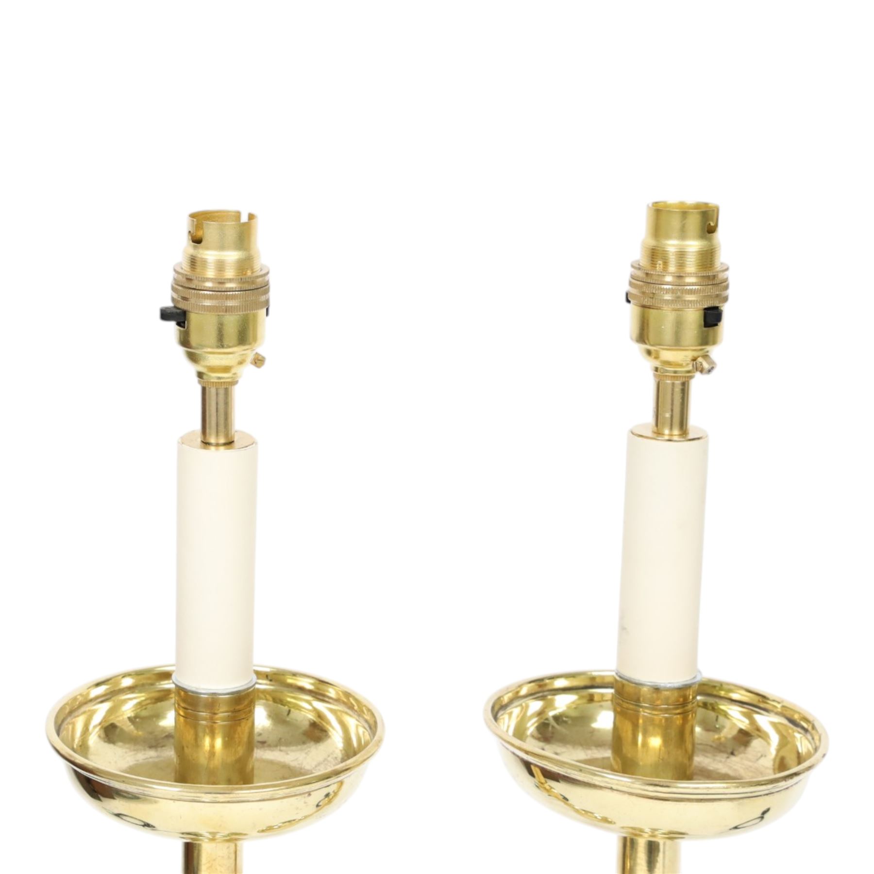Pair of early 20th century brass alter candlesticks converted to table lamps, each with stepped and spreading circular base leading to a double hexagonal knopped column, and plain socket above inverted domed circular drip pan, the socket with light fitting, overall H49cm
