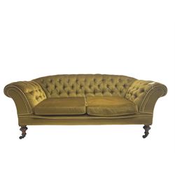 Victorian walnut framed two seat sofa, upholstered in buttoned  olive green fabric with sprung seat and scrolled arms, raised on turned supports with ceramic castors