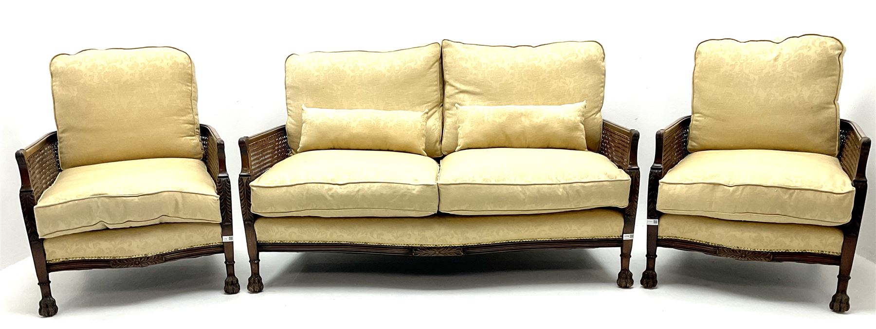 Early 20th century mahogany framed Bergere settee, double cane sides with acanthus carved arms on hairy paw feet, upholstered in a pale gold fabric (W145cm) and two matching armchairs (W66cm)