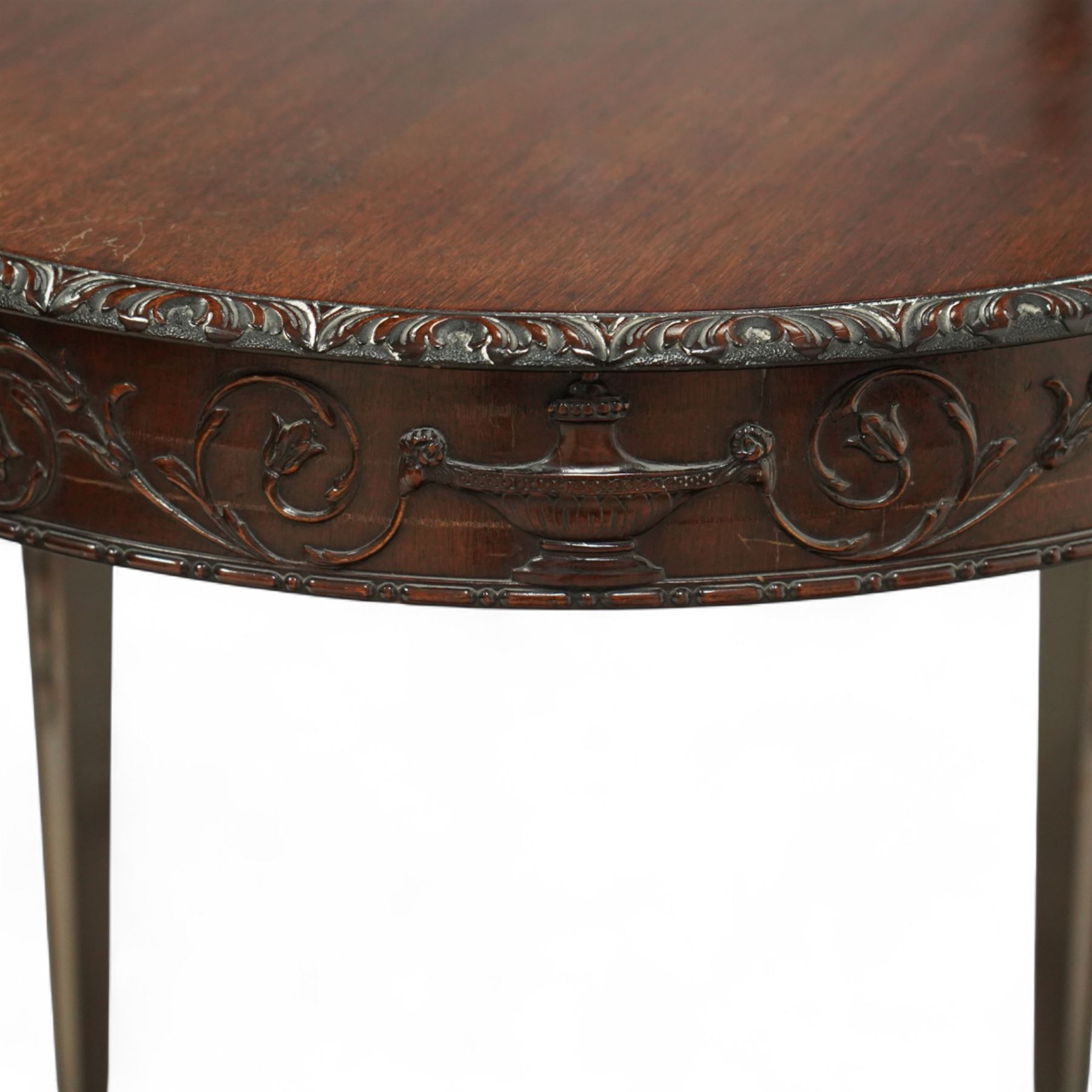 Early 20th century mahogany circular centre table in the Adams style, the moulded frieze carved with scrolling foliage and urn motifs between rosettes, raised on square tapering legs with carved husk decoration and terminating in spade feet