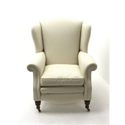Georgian style high wing back armchair, upholstered in cream fabric, turned supports on castors