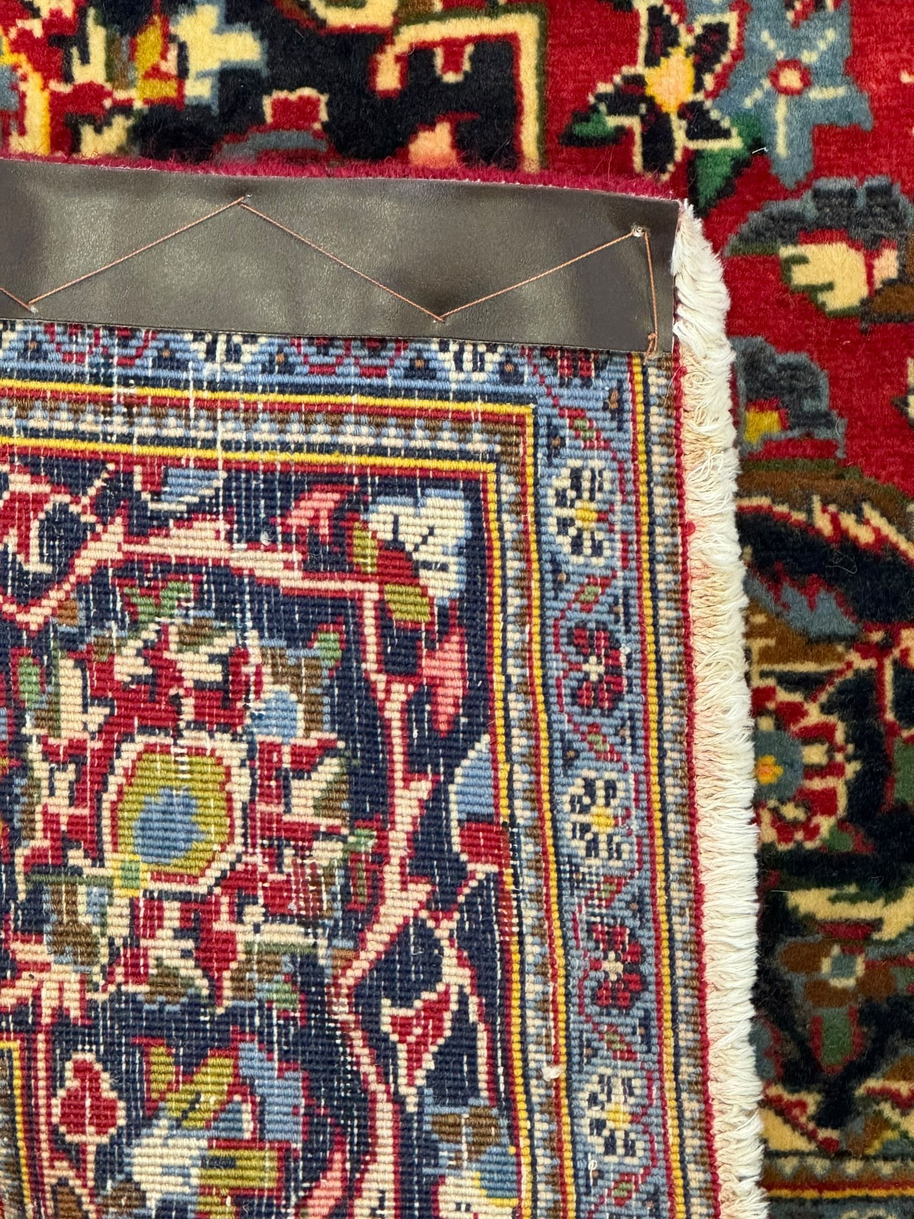 Central Persian Kashan crimson ground rug, central indigo pole medallion surrounded by sparsely placed bouquets interconnected with foliate branches, the guarded border with repeating palmette and Boteh motifs with interwoven scrolling patterns, framed by guard stripes