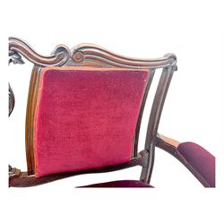 Late Victorian stained beech framed sofa, the backrests, seat and padded arms upholstered in deep red fabric, carved crest rail with scroll and foliate motifs supported by carved uprights, on cabriole supports with leaf carvings terminating in castors