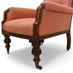 Victorian mahogany framed armchair, upholstered in salmon pink dot patterned fabric, the moulded arms with carved scroll terminals, raised on turned and fluted front legs and swept back legs, all with castors