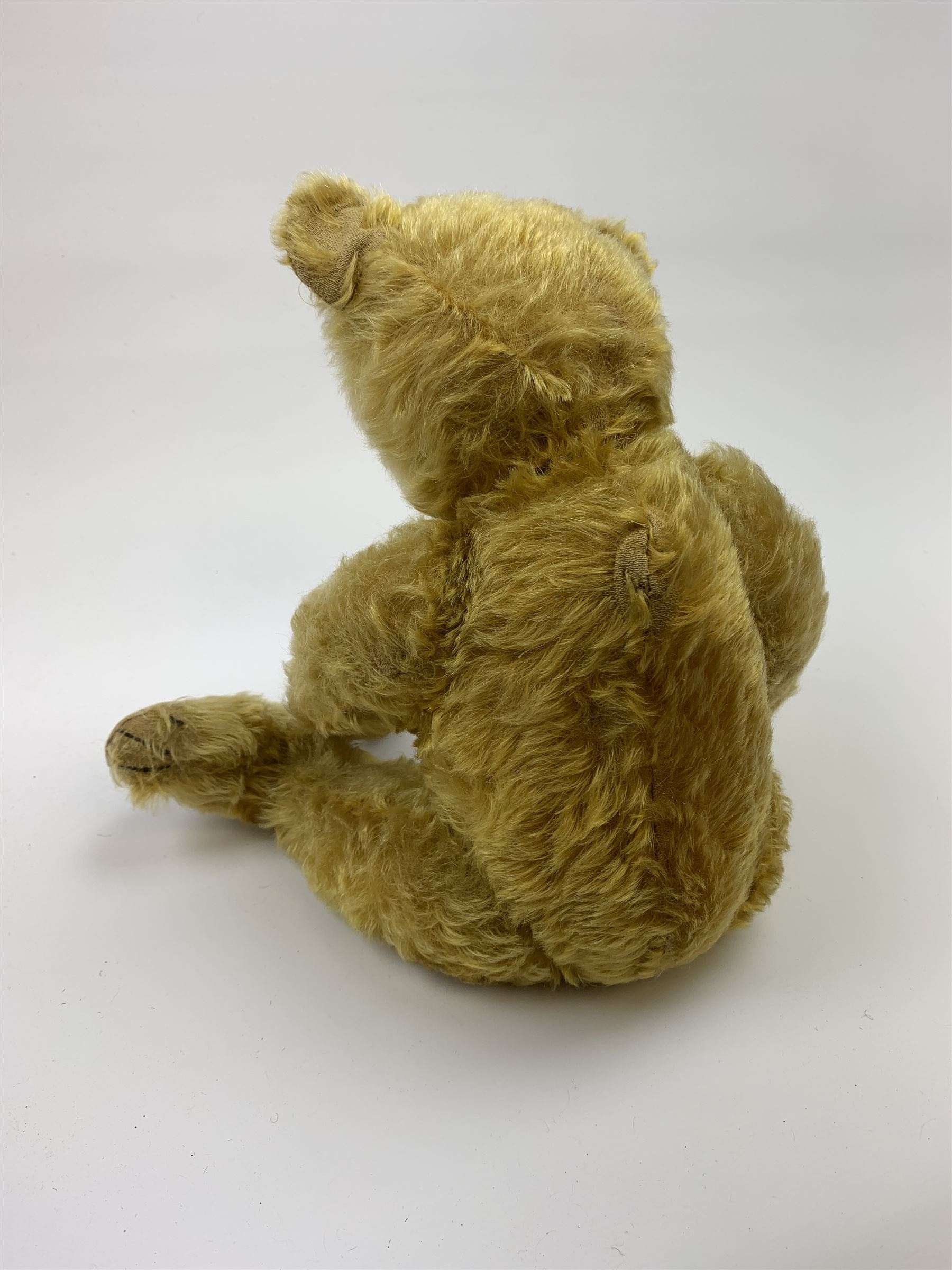 Early 20th century German teddy bear c1920, probably Steiff or Bing, with wood wool filled humped back golden mohair body, swivel jointed head with glass eyes and brown vertically stitched nose and mouth, jointed limbs with elongated arms and felt paw pads with black stitched claws H18