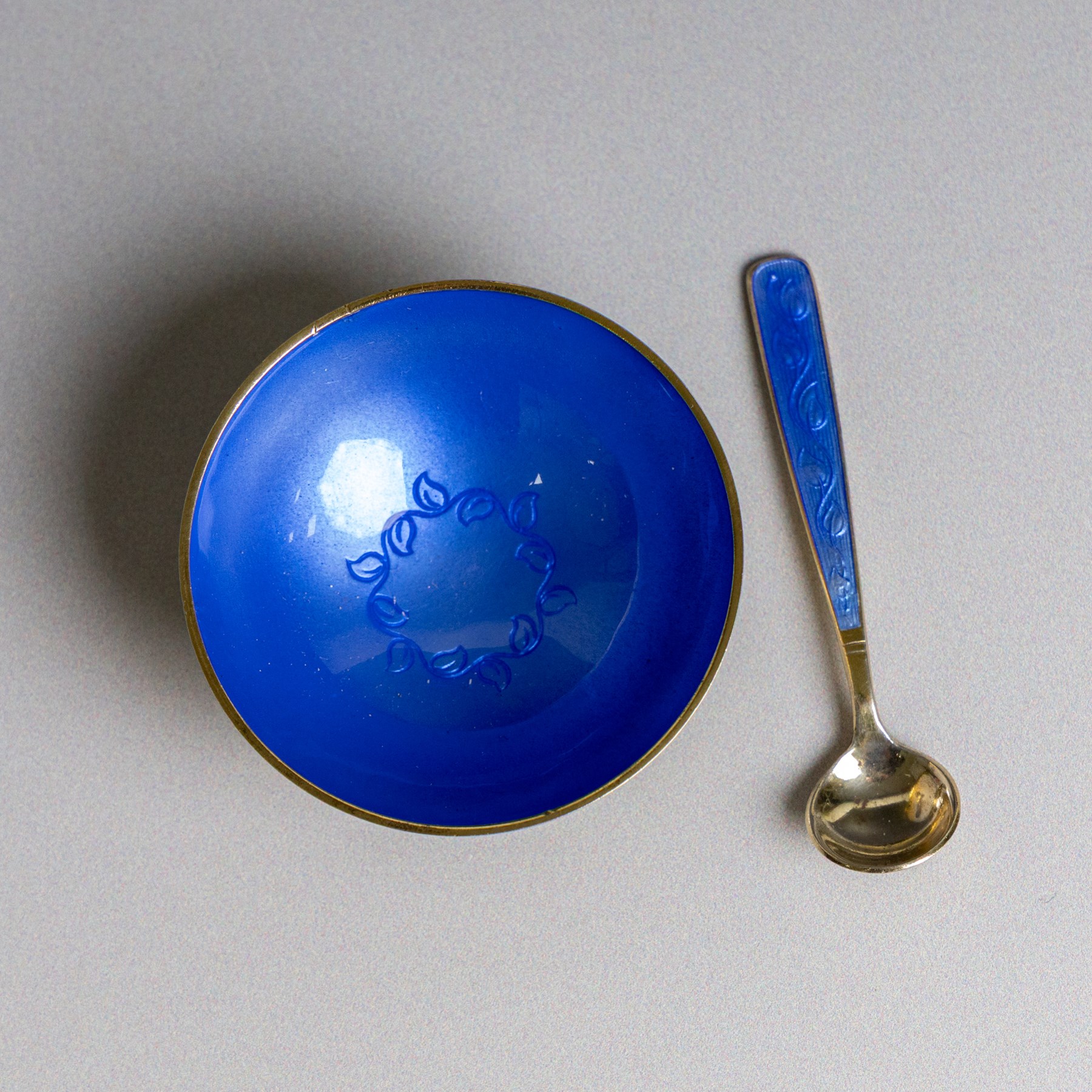 Mid 20th century Danish silver-gilt and guilloche enamel cruet set by Volmer Bahner, comprising pepper shaker, open salt and salt spoon, the spoon handle and bowl interior with blue basse taille enamel and vine motif, the pepperette with panels of blue guilloche enamel with similar applied vine decoration, all stamped Sterling Denmark VB, pepperette H4cm