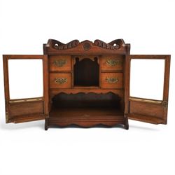 19th century oak table top smokers cabinet, with carved foliate pediment, the two beveled edge glass doors opening to reveal a fitted interior, with four drawers and fitted brass of pipe holders to each door, H46cm