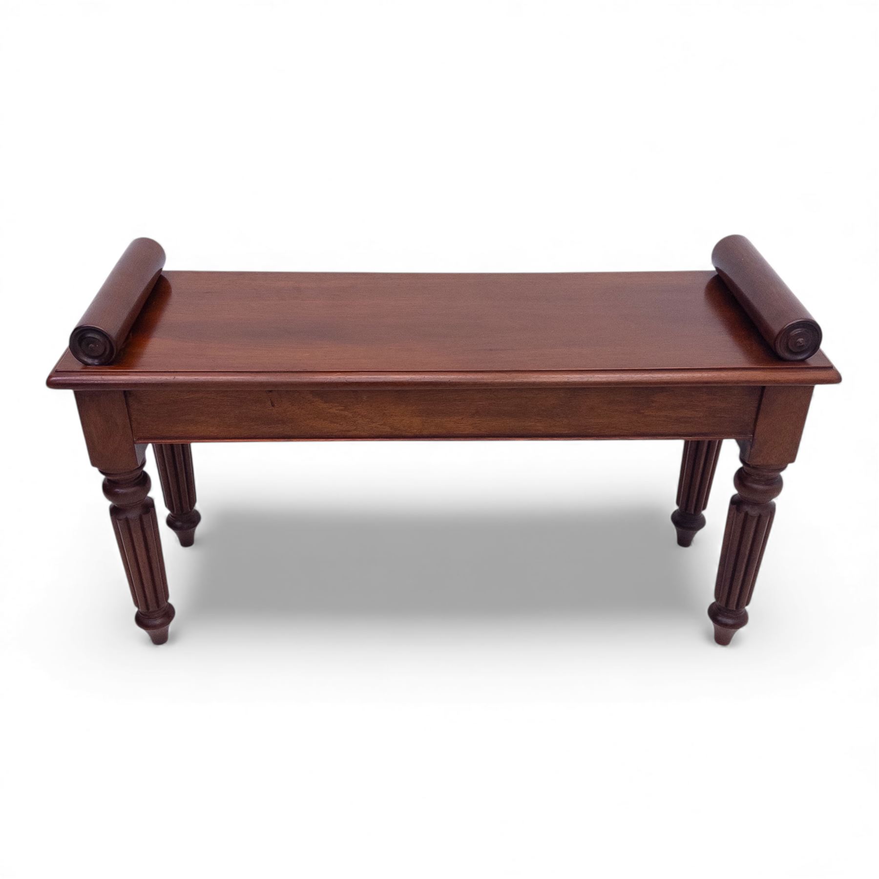 Regency style mahogany window seat, in the manner of George Bullock, with rectangular top with twin scroll ends, raised on four turned and reeded supports terminating in bun feet