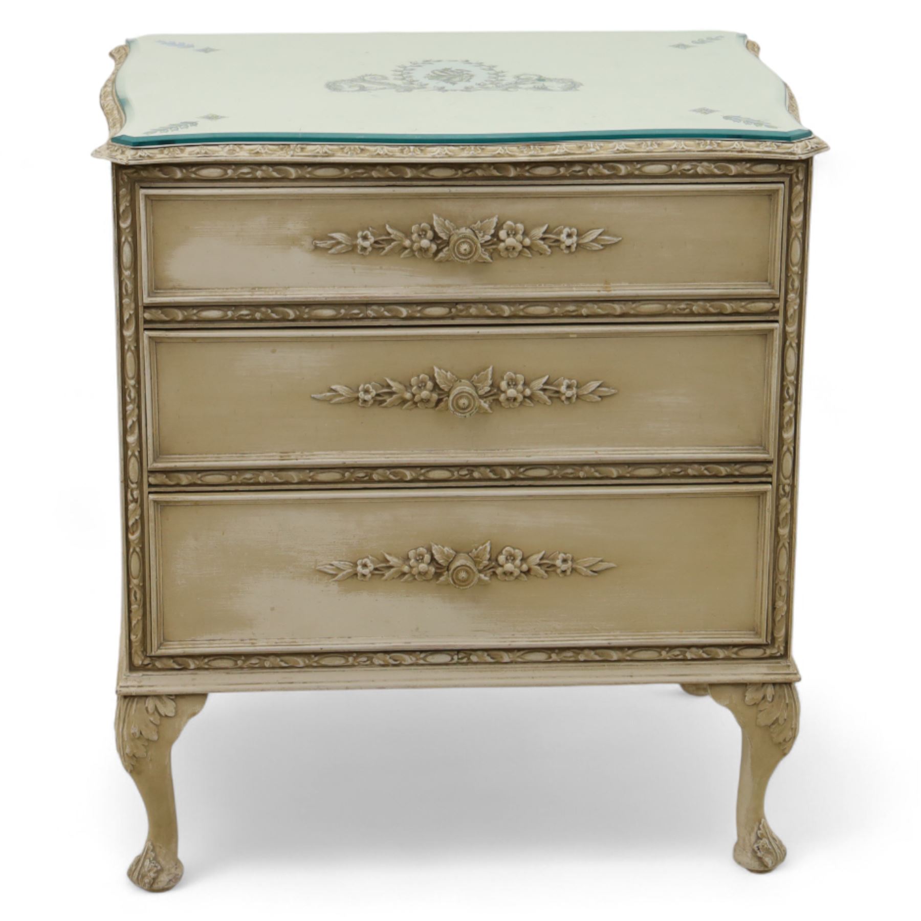 French design cream painted three drawer commode, shaped front with floral garland appliqués, fluted uprights and acanthus carved cabriole legs terminating in scroll feet