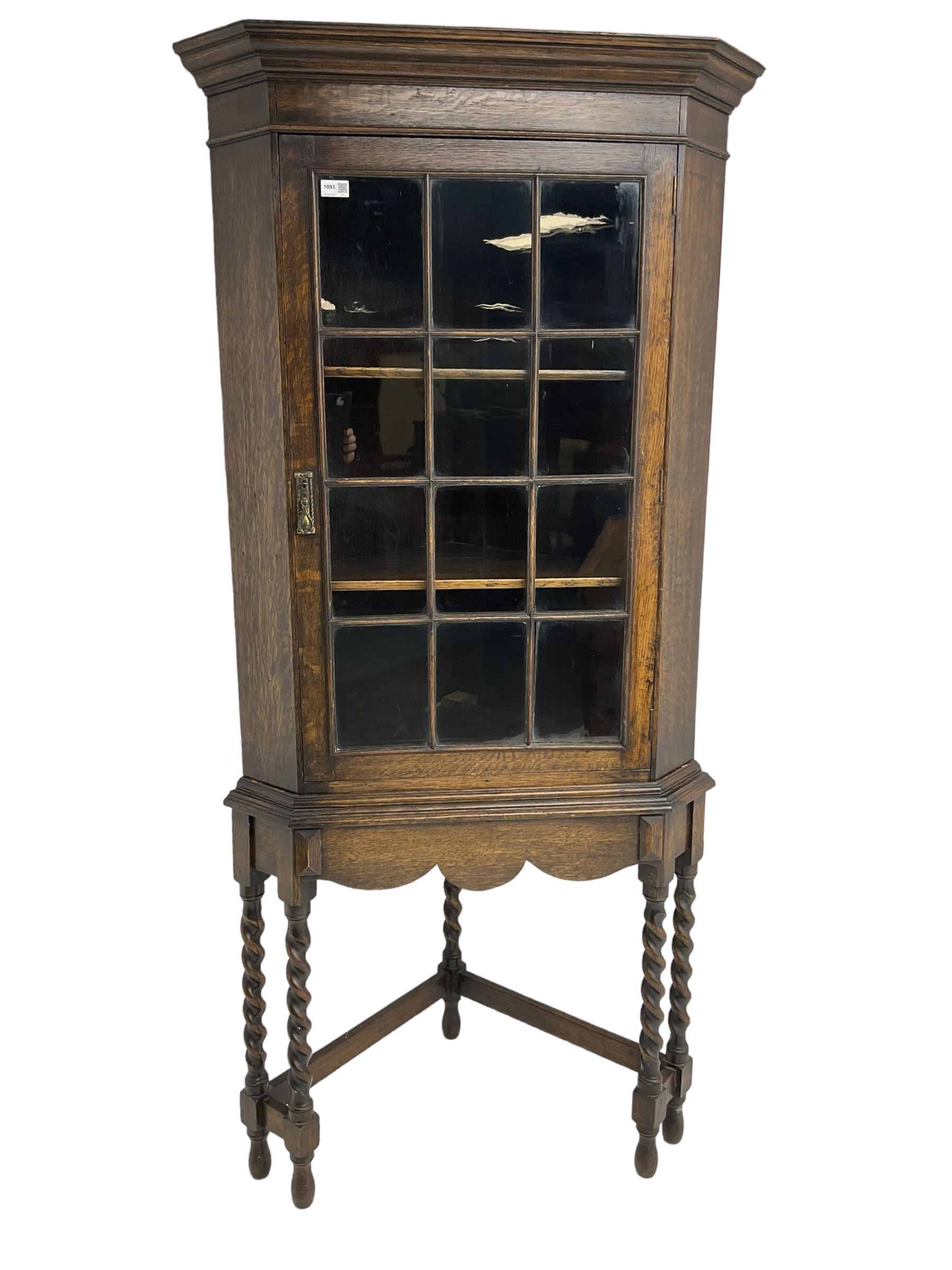 Early to mid-20th century oak corner display cabinet, projecting cornice over astragal glazed door, on spiral turned supports joined by stretchers
