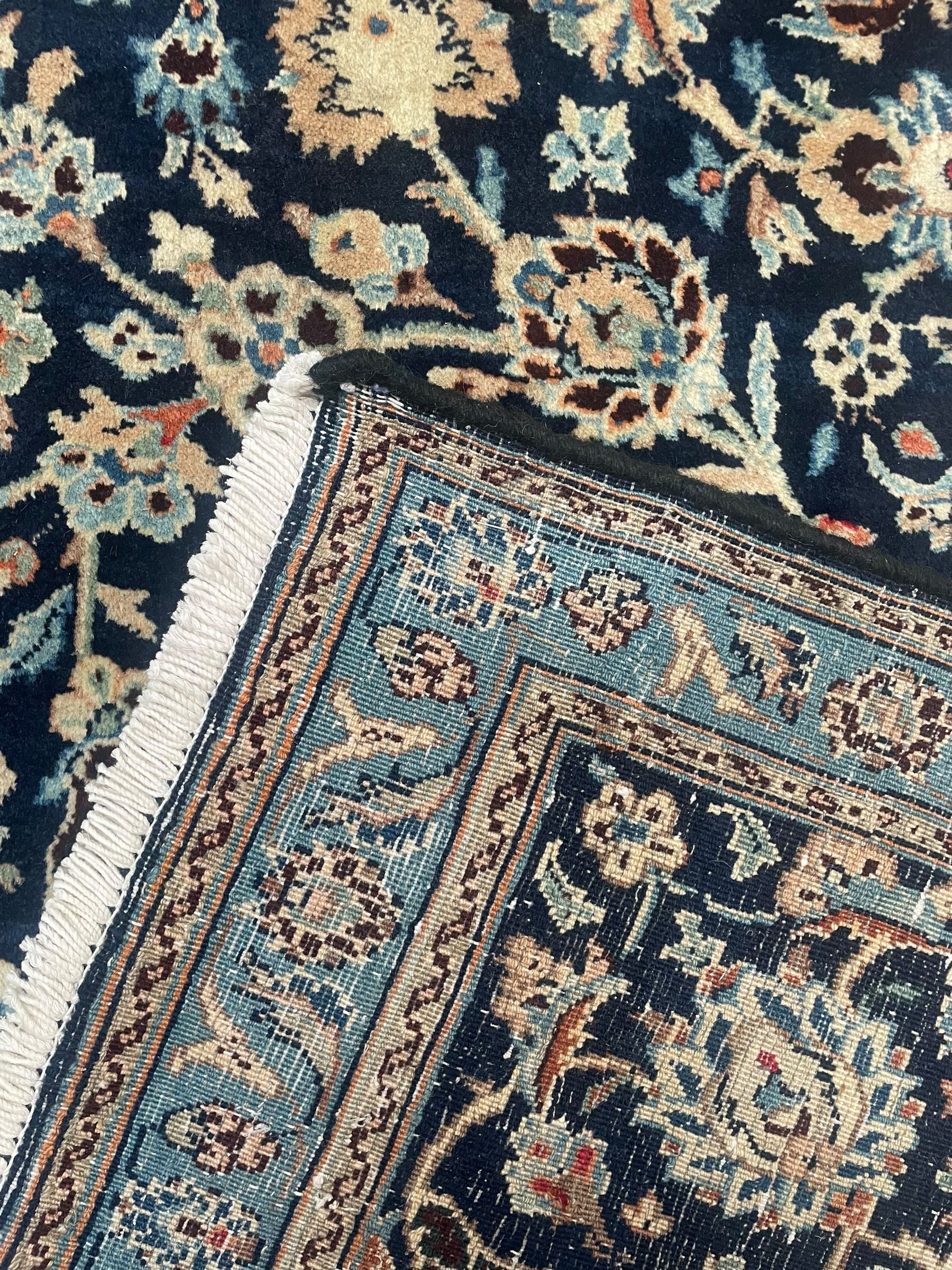 Persian Kashan indigo ground rug, the rosette medallion decorated with projecting palmettes, on a field of swirling leafy branches and decorated with further palmettes, the scrolling border with repeating stylised plant motifs, within floral pattern guard stripes