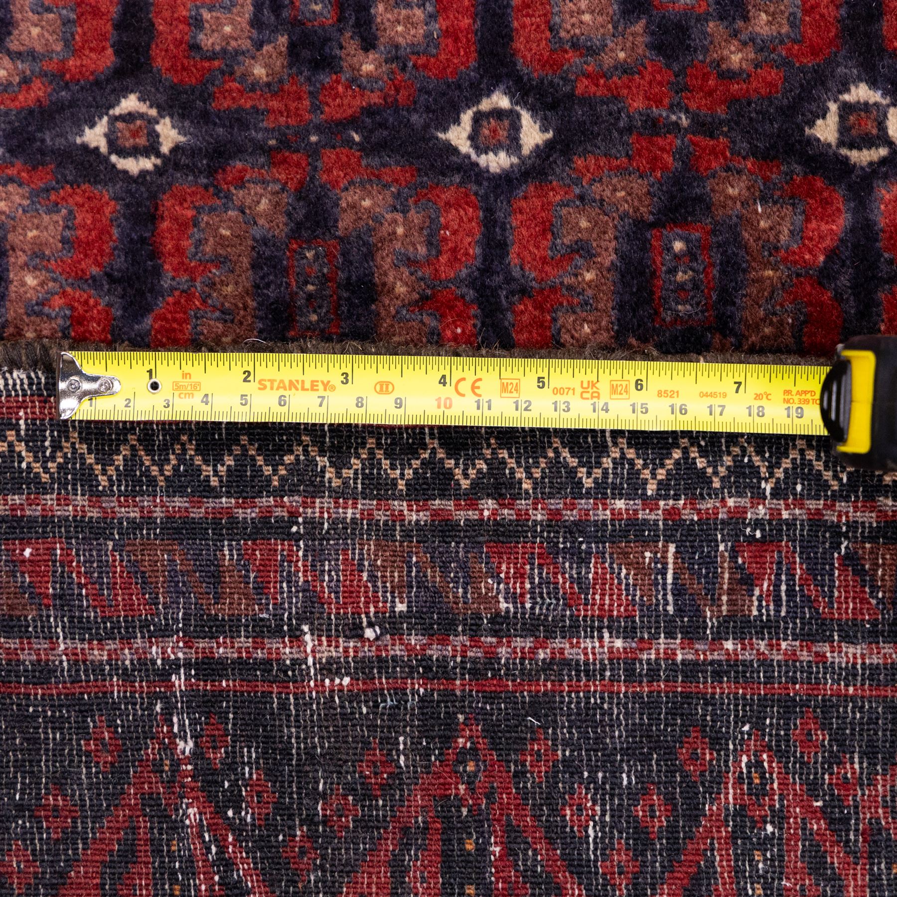 North East Persian Turkoman hand-knotted rug, indigo field densely decorated with an all-over repeating design of geometric gul motifs in shades of madder red, aubergine, and dark brown, highlighted with small ivory details, framed by multiple narrow guard borders and a main border with angular geometric motifs flanked by zig-zag borders, with cotton fringe ends 