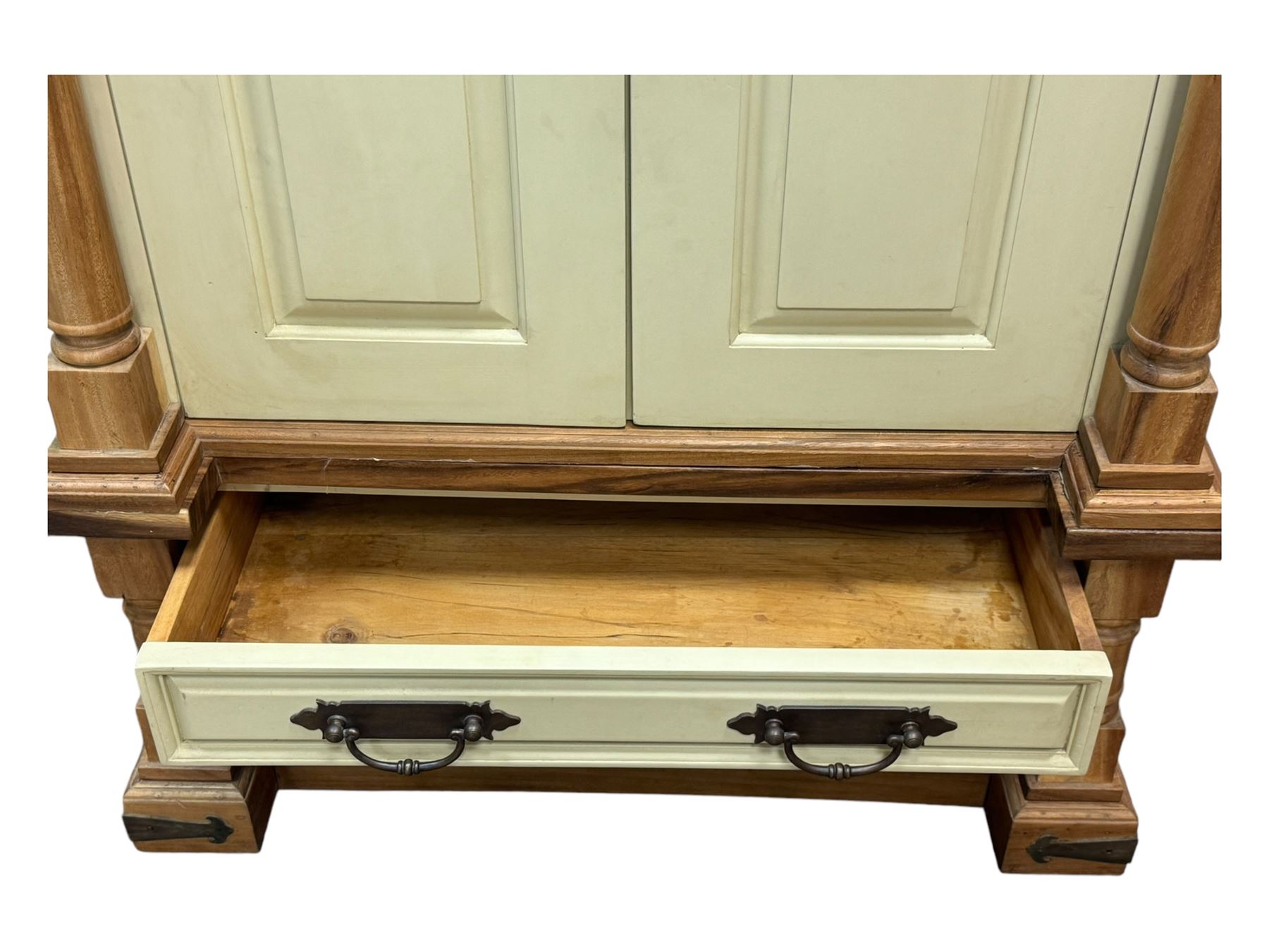 Hardwood and cream painted kitchen larder cupboard, sloped pediment over two panelled doors, the interior fitted with slides, drawers and storage shelves, two long drawers below, mounted by turned pilasters, on metal bound moulded plinth base