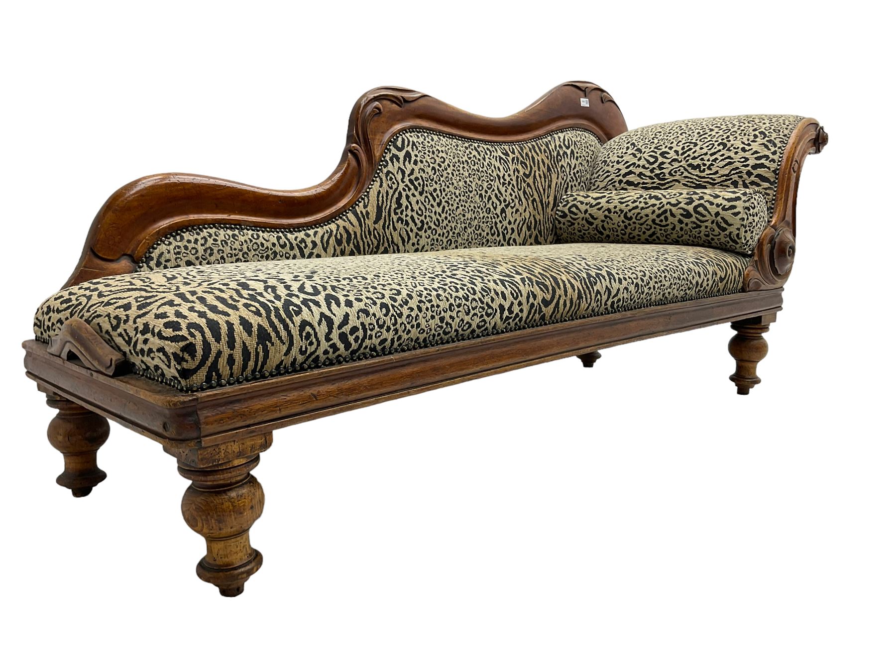 Victorian mahogany framed chaise longue, shaped arm carved with acanthus leaves, the scrolled back with applied carved rosettes,upholstered in monochrome leopard print fabric with bolster cushion, raised on turned supports