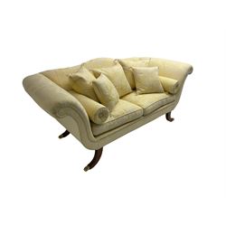 Regency design two seat sofa, serpentine back with scrolled arms, upholstered in pale yellow damask fabric, raised on reeded sabre supports terminating in brass hairy paw feet, with two bolster and five scatter cushions