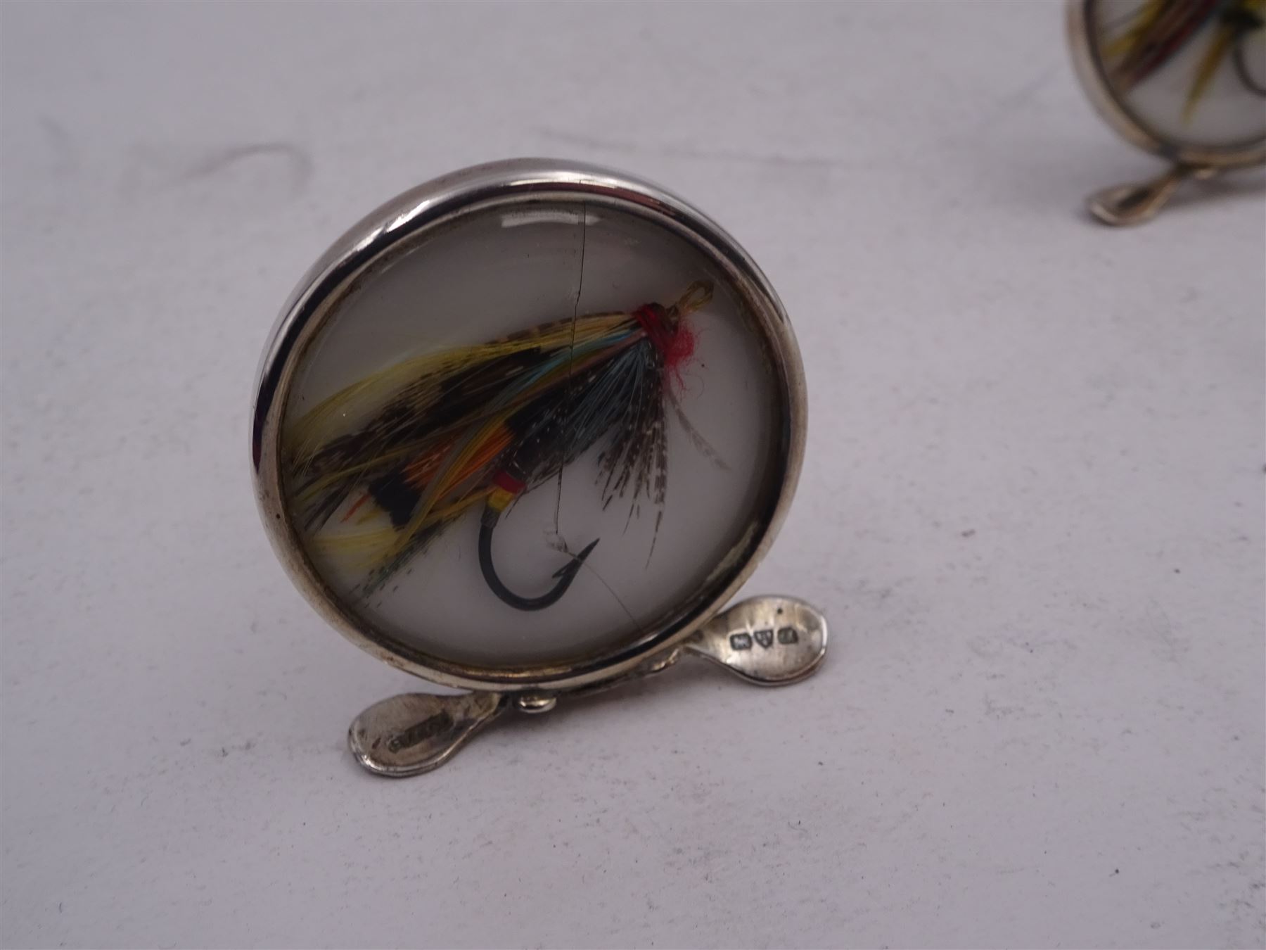 Set of four early 20th century silver mounted place card holders, each of circular form and set with a coloured fly fishing hook behind a glazed panel, upon three pad feet, hallmarked Grey & Co, Chester 1912, H4.5cm, contained within red fitted case, with purple silk and velvet interior