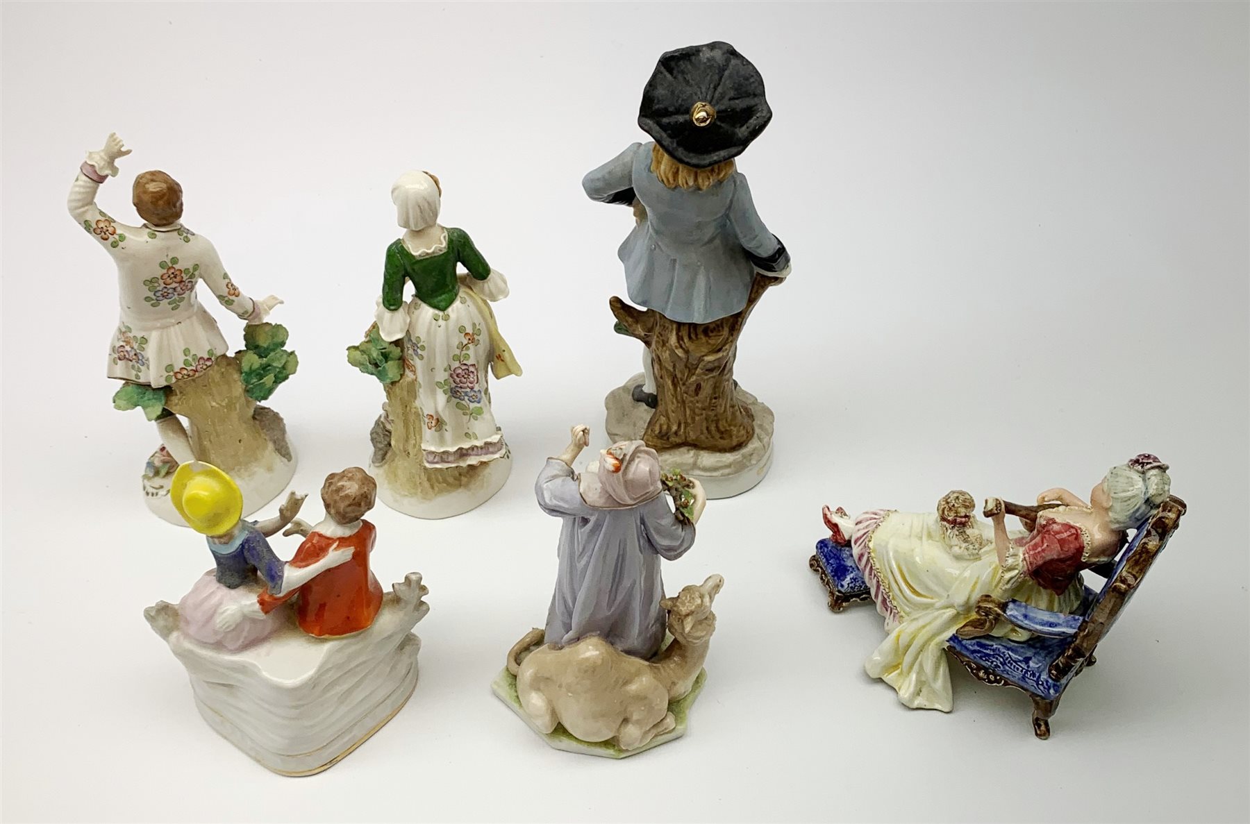 A pair of Sitzendorf figures, modelled as a male and female figure in eighteenth century dress with sheep beside feet, each upon gilt detailed circular base, each with printed mark beneath, tallest H18.5cm, together with a Volkstedt figure modelled as a Eastern female figure with camel seated at her feet, with printed mark beneath, a Sitzendorf figure of a young male figure, a figure modelled as a seated female playing the lute, with dog seated upon her lap, and a figure group marked foreign. (6). 